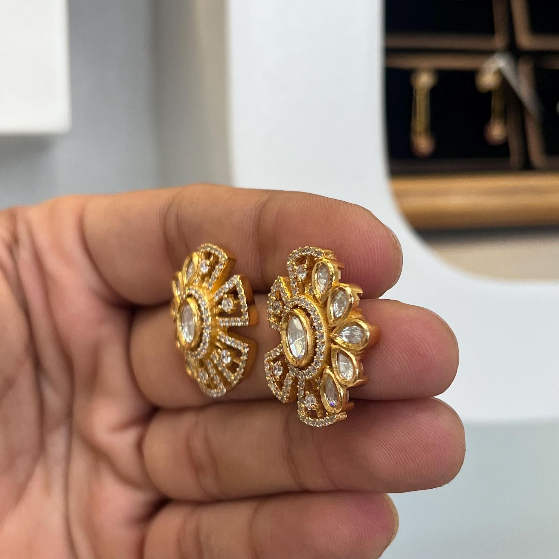 Gold earrings held in a hand with a blurred background