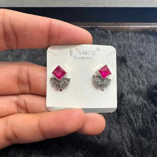Silver earrings with pink gemstones on a branded card held by a hand.